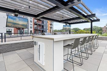 A white outdoor bar with a row of chairs and a screen tv.
